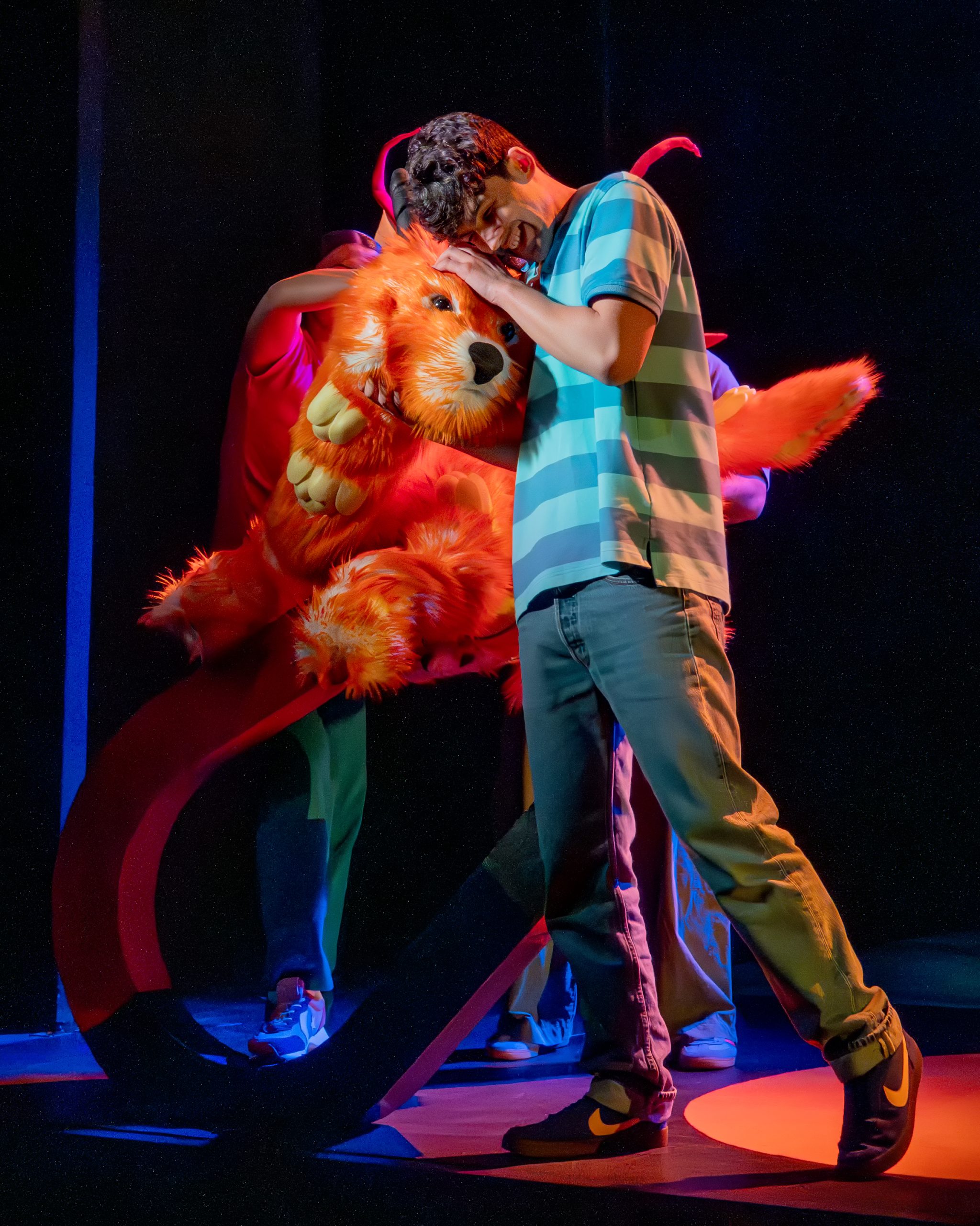 a theatre show production image of a young boy hugging an orange dog like creature