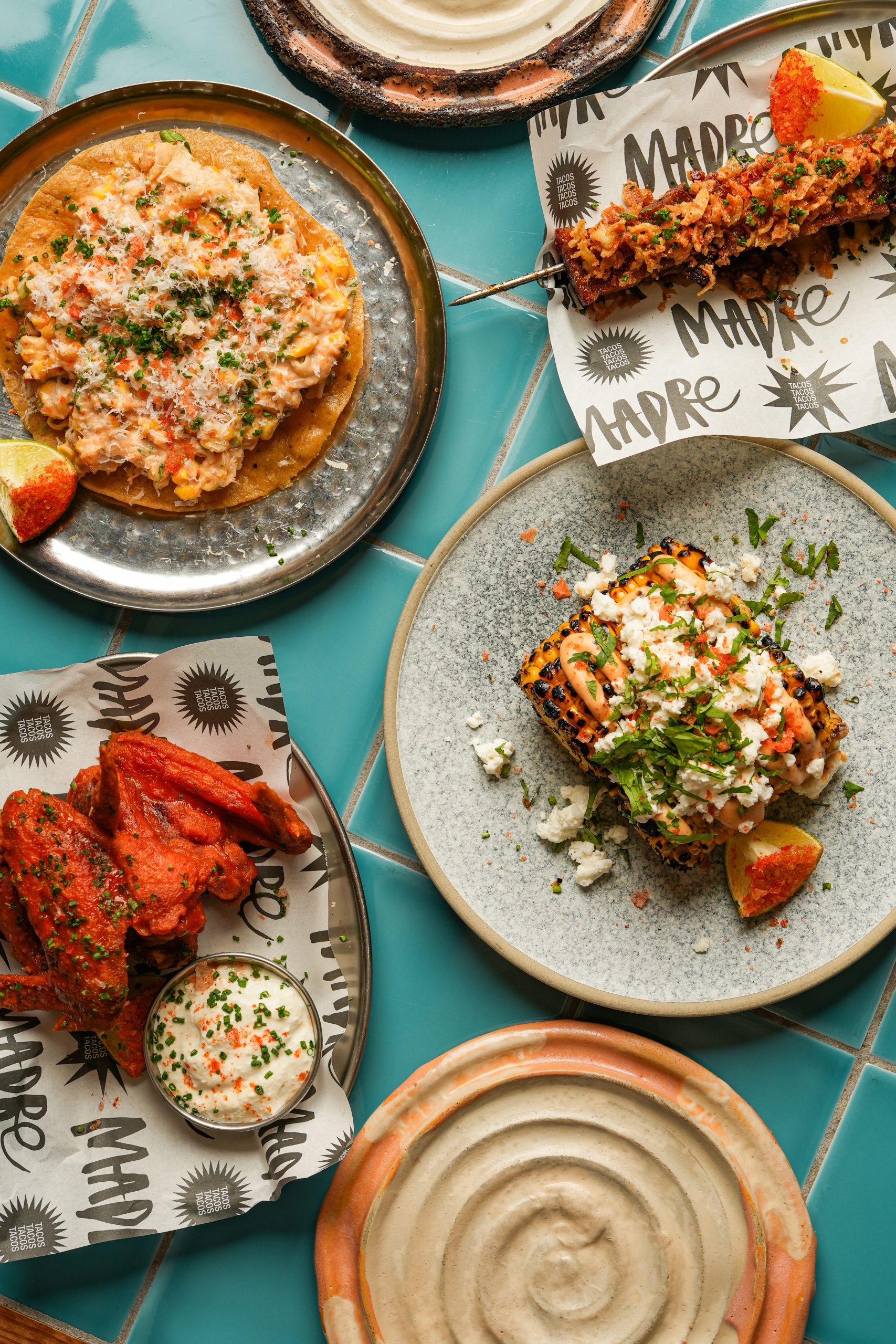 a table top view of several plates of food including chicken wings and a flatbread