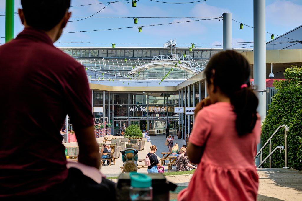 families sat outside in the courtyard of a shopping centre with benches and grass