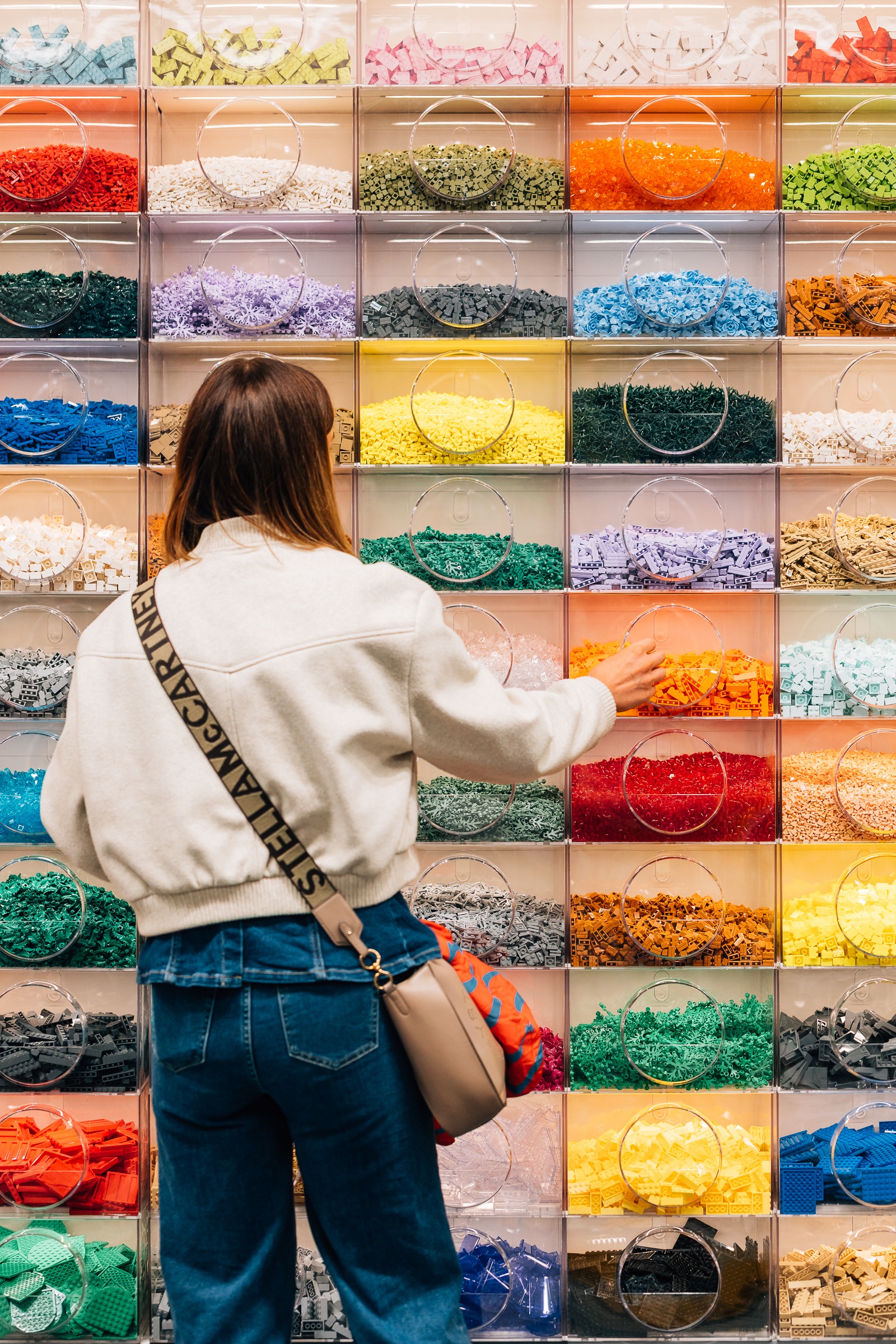 a person standing in front of a wall with compartments filled with lego pieces, divided by colour and size