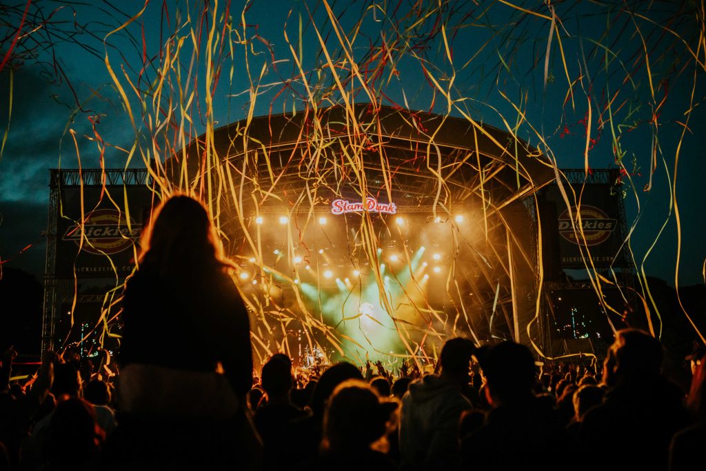a nighttime shot at an outdoor music festival with the stage lit up, people watching and streamers falling across the crowd
