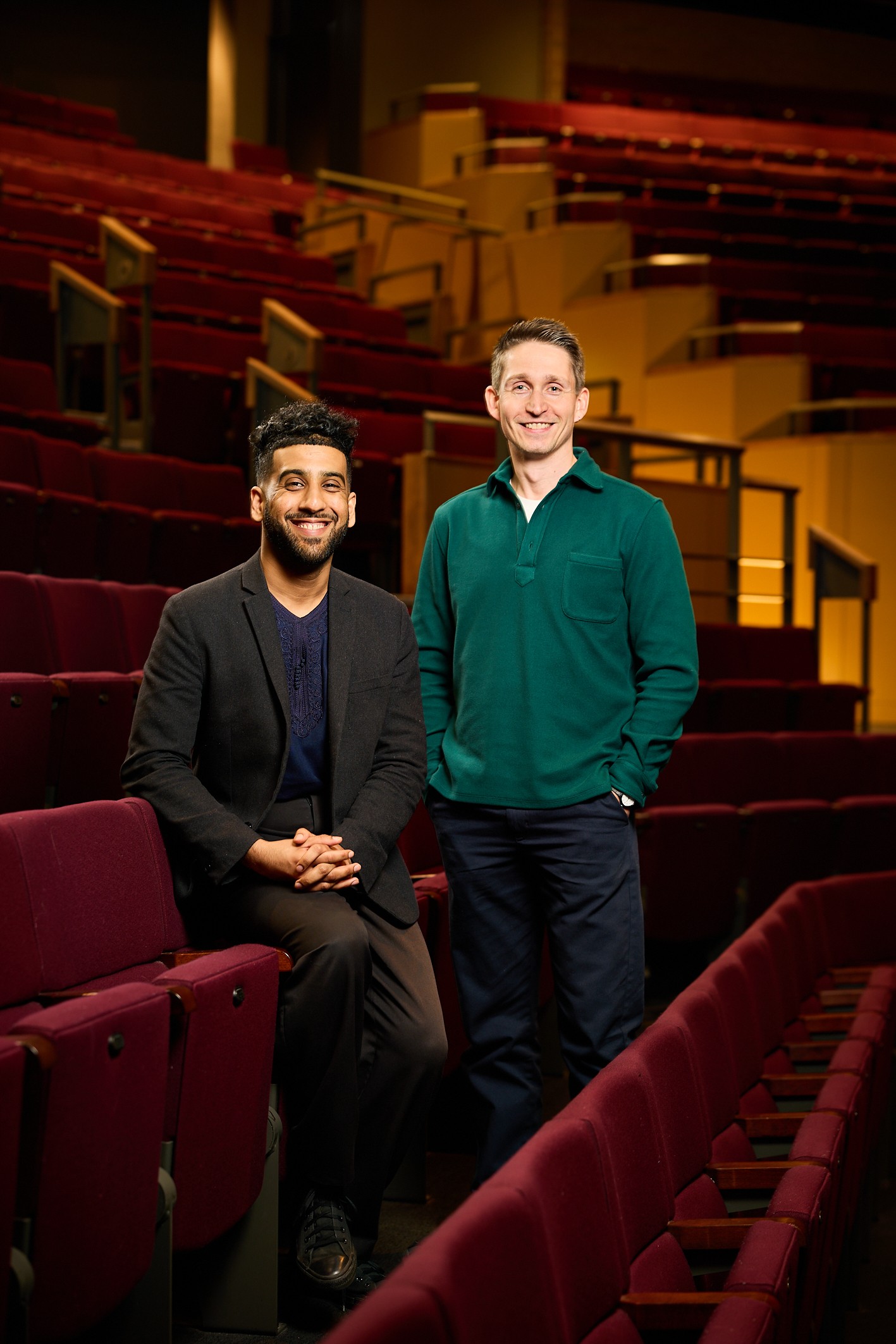 two people stood inside a theatre seating area looking at the camera