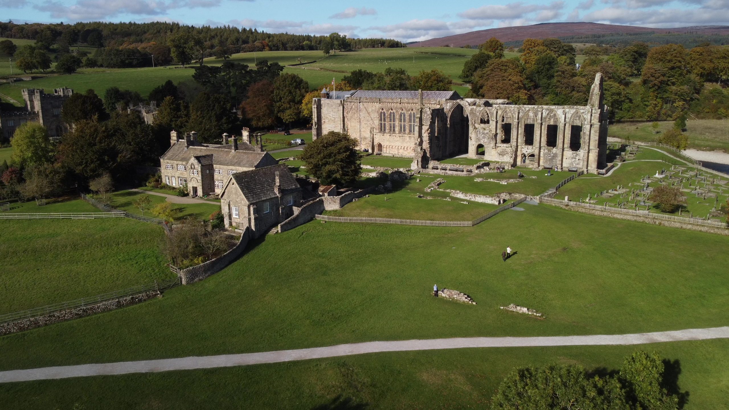 an aerial view of a ruined abbey in a green field with a large stone home next to it