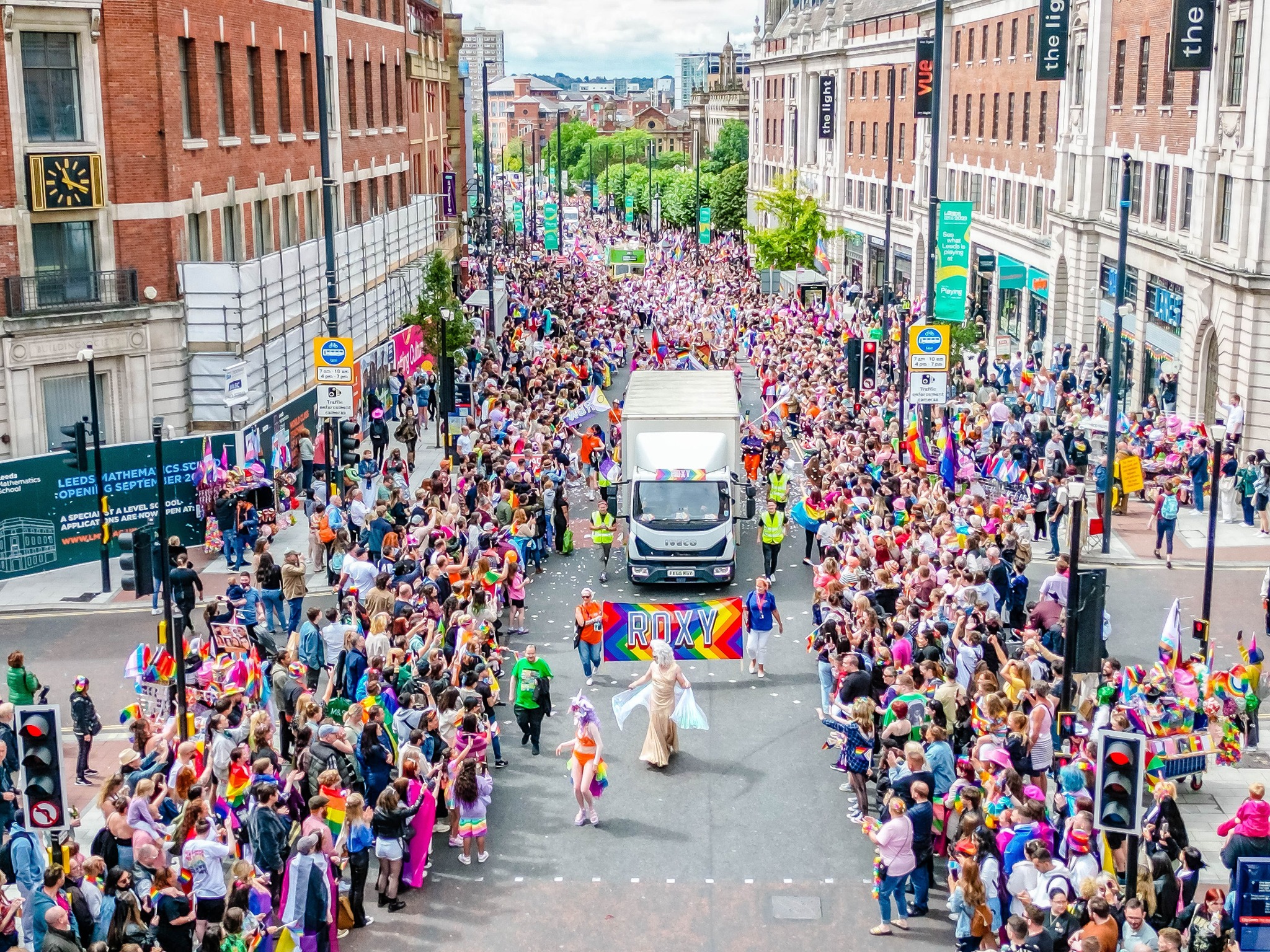a parade on a city street with a drag queen being followed by parade goers