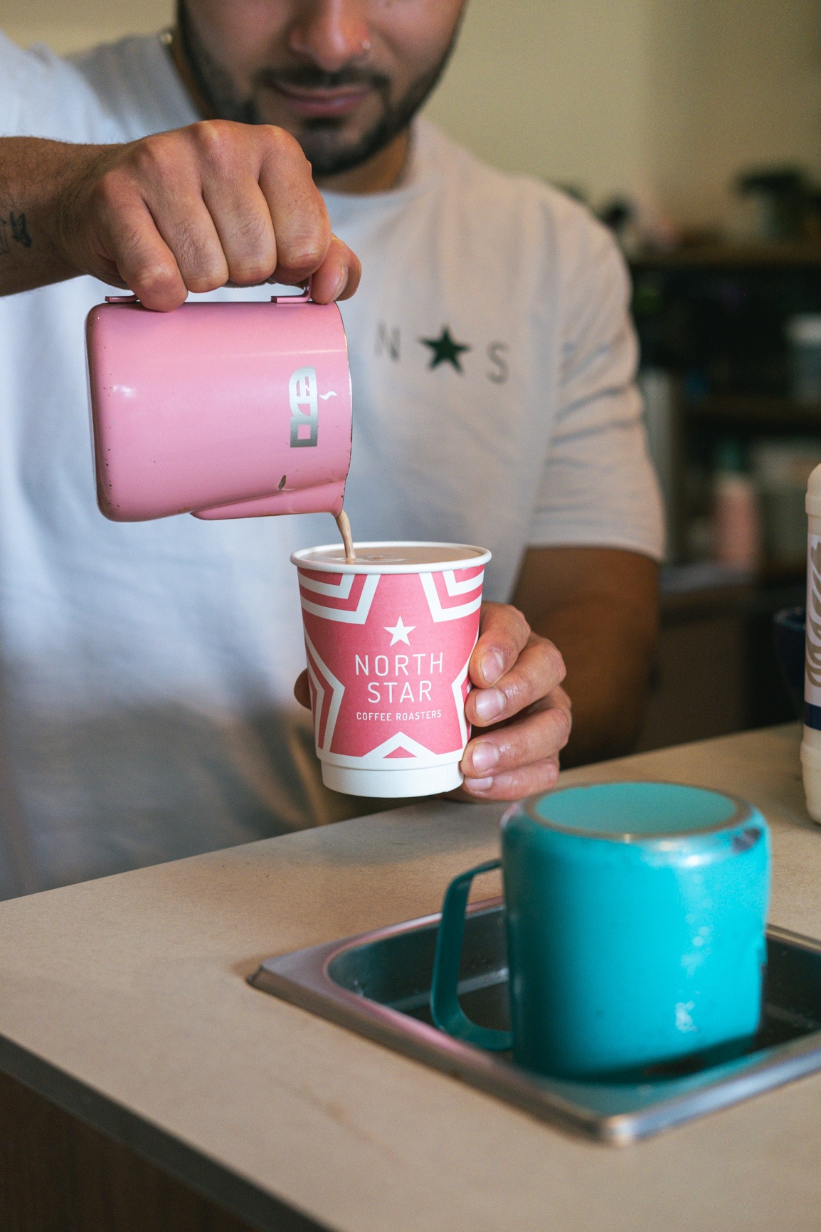 a barista pouring from a colourful jug into a north star branded coffee cup