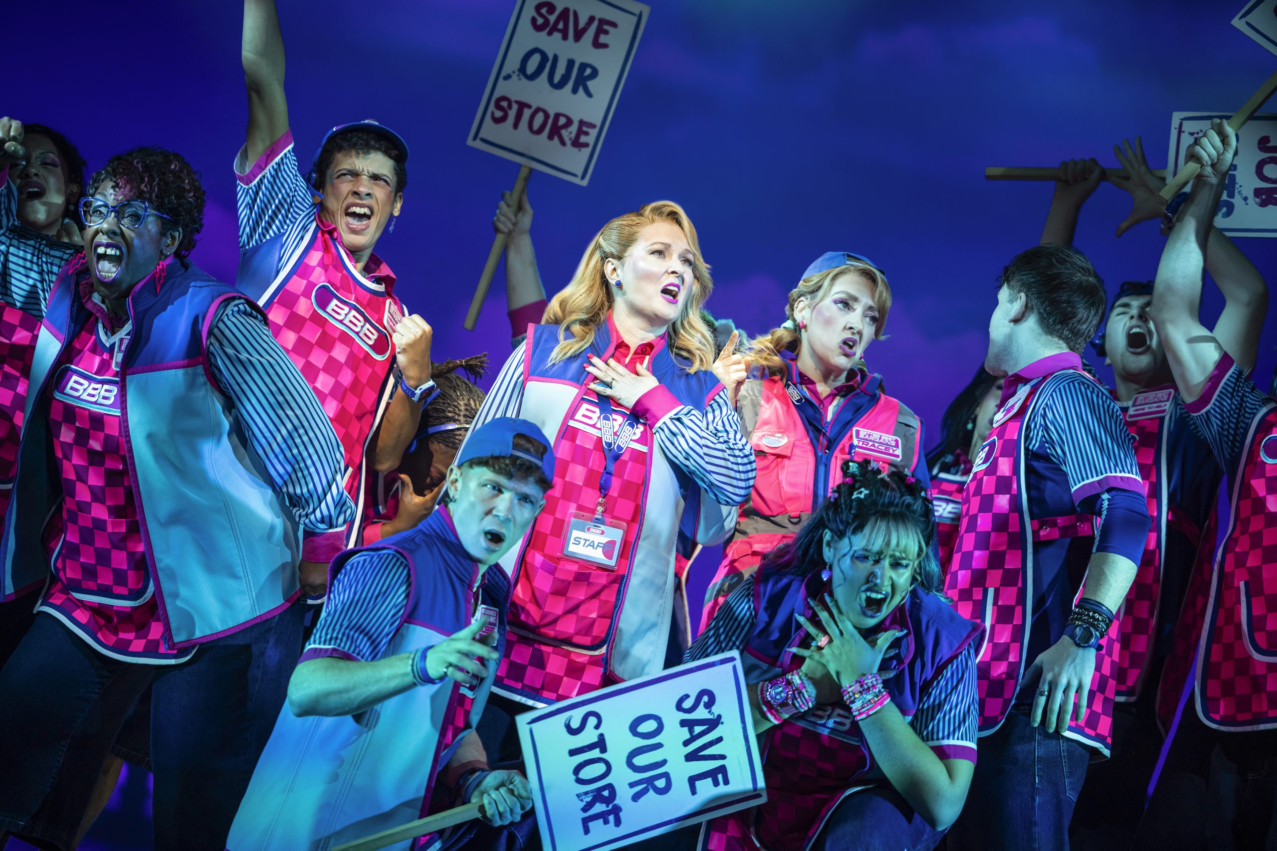 a troupe of actors on a theatre stage holding signs saying save our store