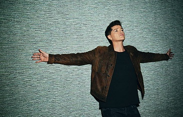 a person with short hair stood in front of a light background holding their arms out beside them