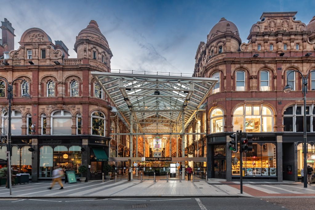 a large shopping centre with two victorian red terracotta buildings side by side with a glass roof in the alley between them 