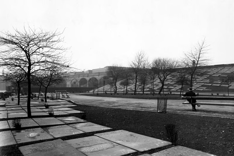 an old black and white photo of a stone path and some trees in between the flags