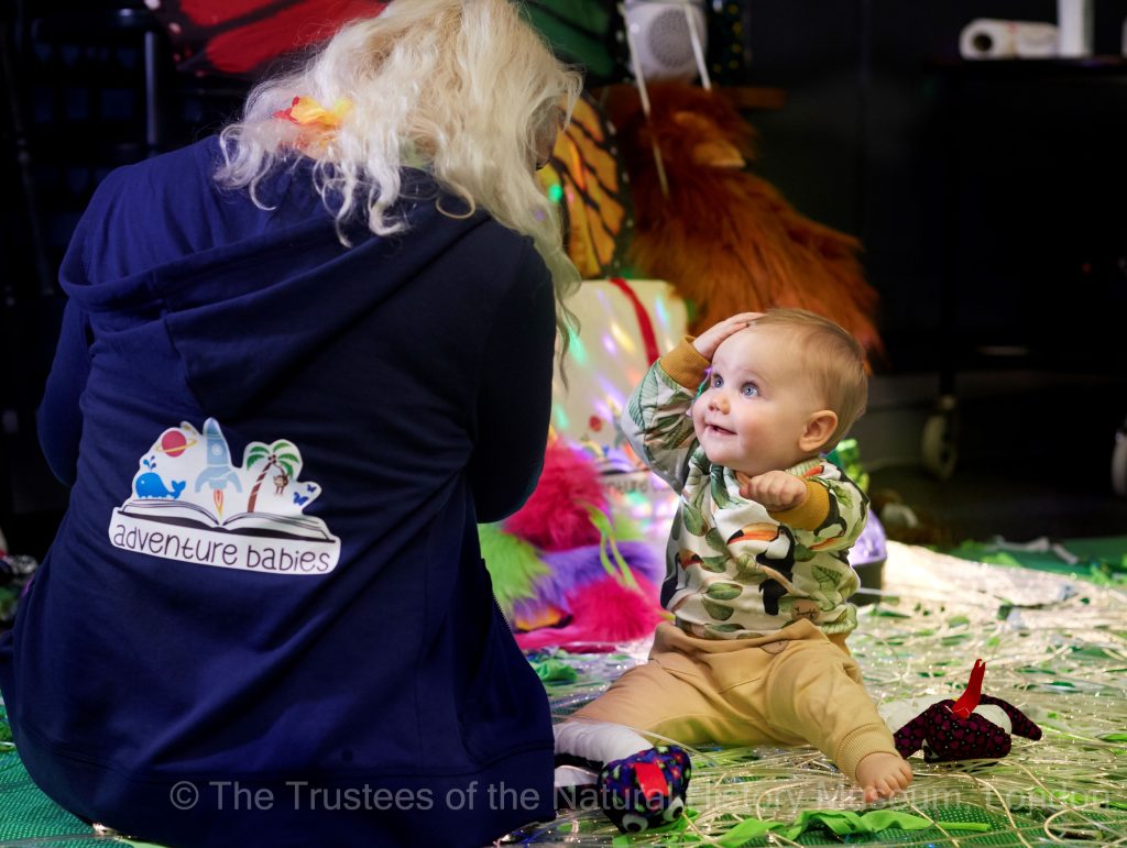 a woman kneeling on the floor playing with a baby and a variety of toys