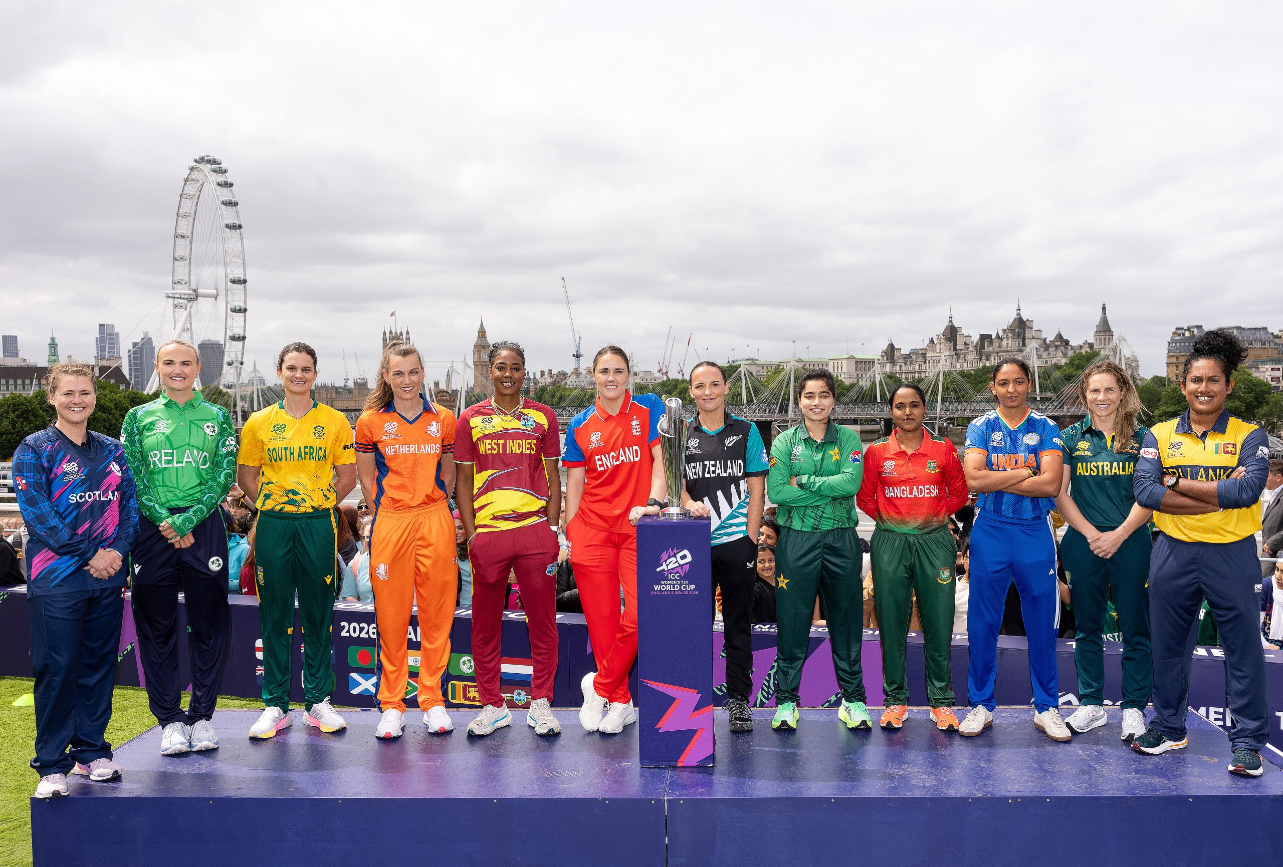 12 women stood side by side on a podium with the london skyline behind them