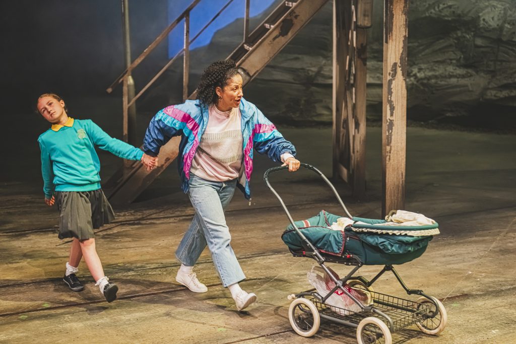 a theatre stage with a woman pushing a pram and holding hands with a young child