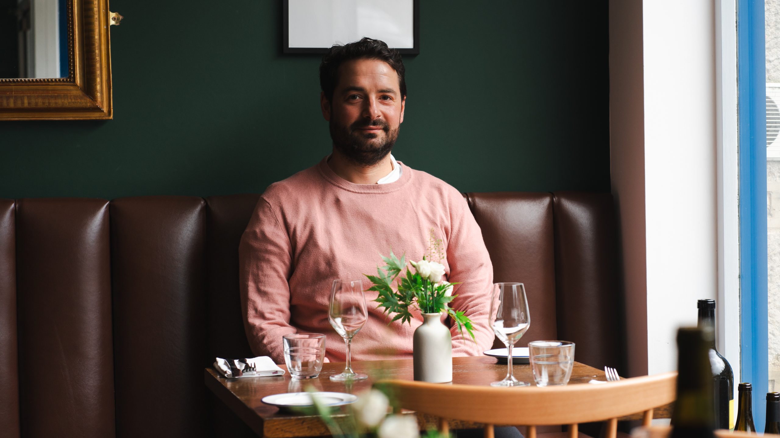 a man sat at a table in a booth seat looking at the camera