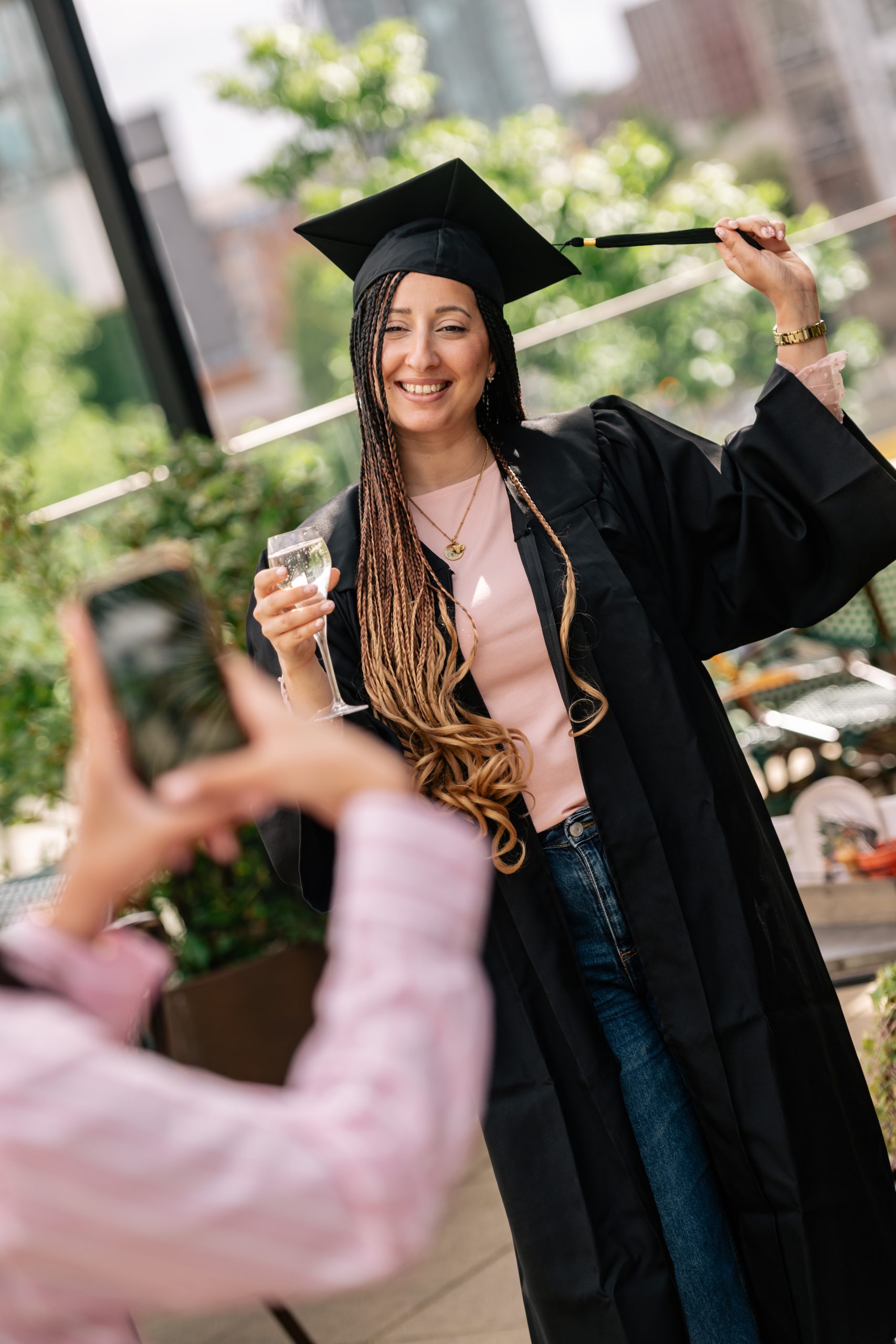 a woman in a graduation gown and cap holding a drink flute, having their photo taken by someone