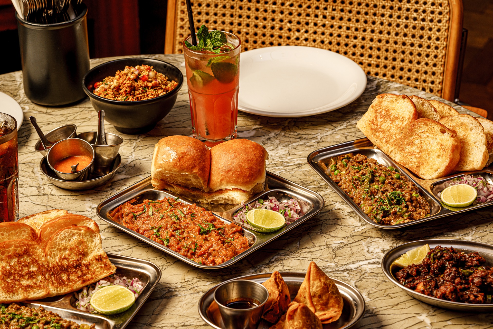 a table filled with plates, bowls and trays of food including currys and rolls