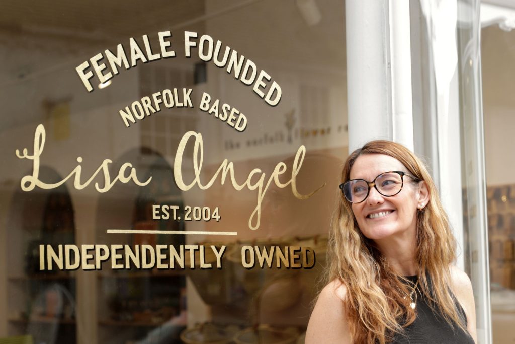 a woman stood by a window with writing on it saying female founded lisa angel independently owned