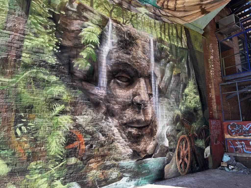 a mural underneath a bridge featuring a rock face with a waterfall and trees surrounding it