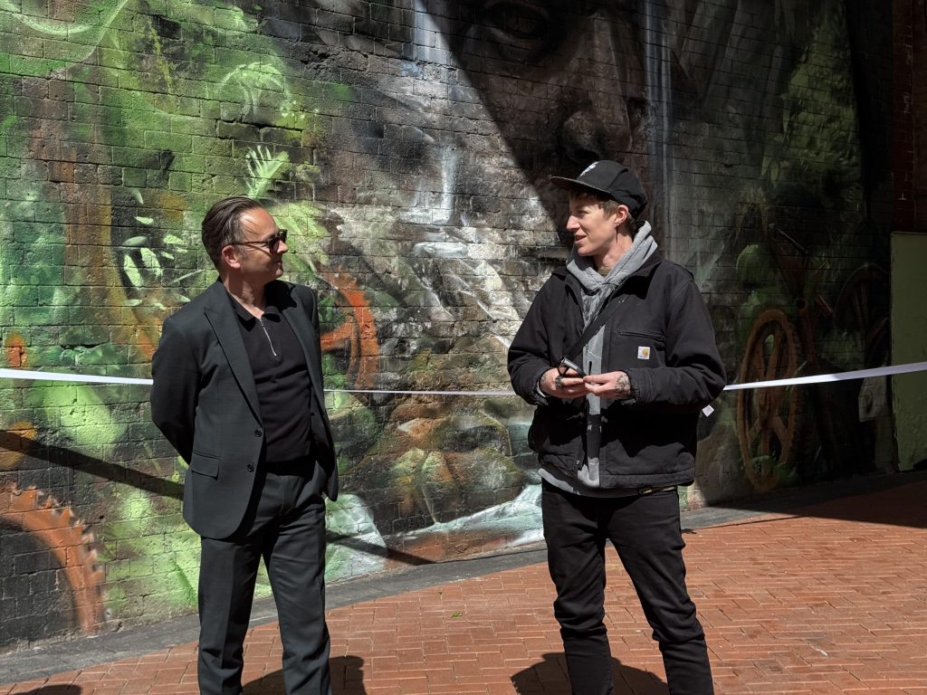 two people stood together in front of a colourful mural on a wall