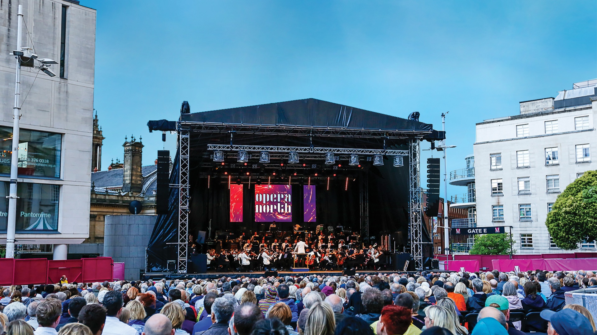 a large stage outdoors with a crowd watching and an orchestra playing on the stage