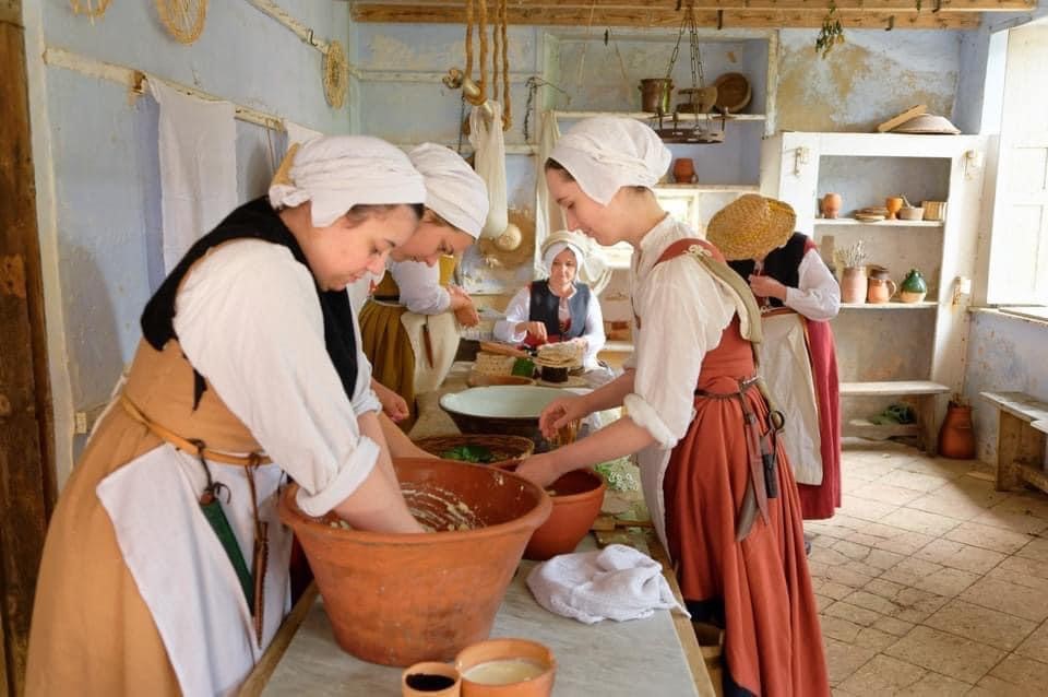 people dress in old period clothing making food in large bowls