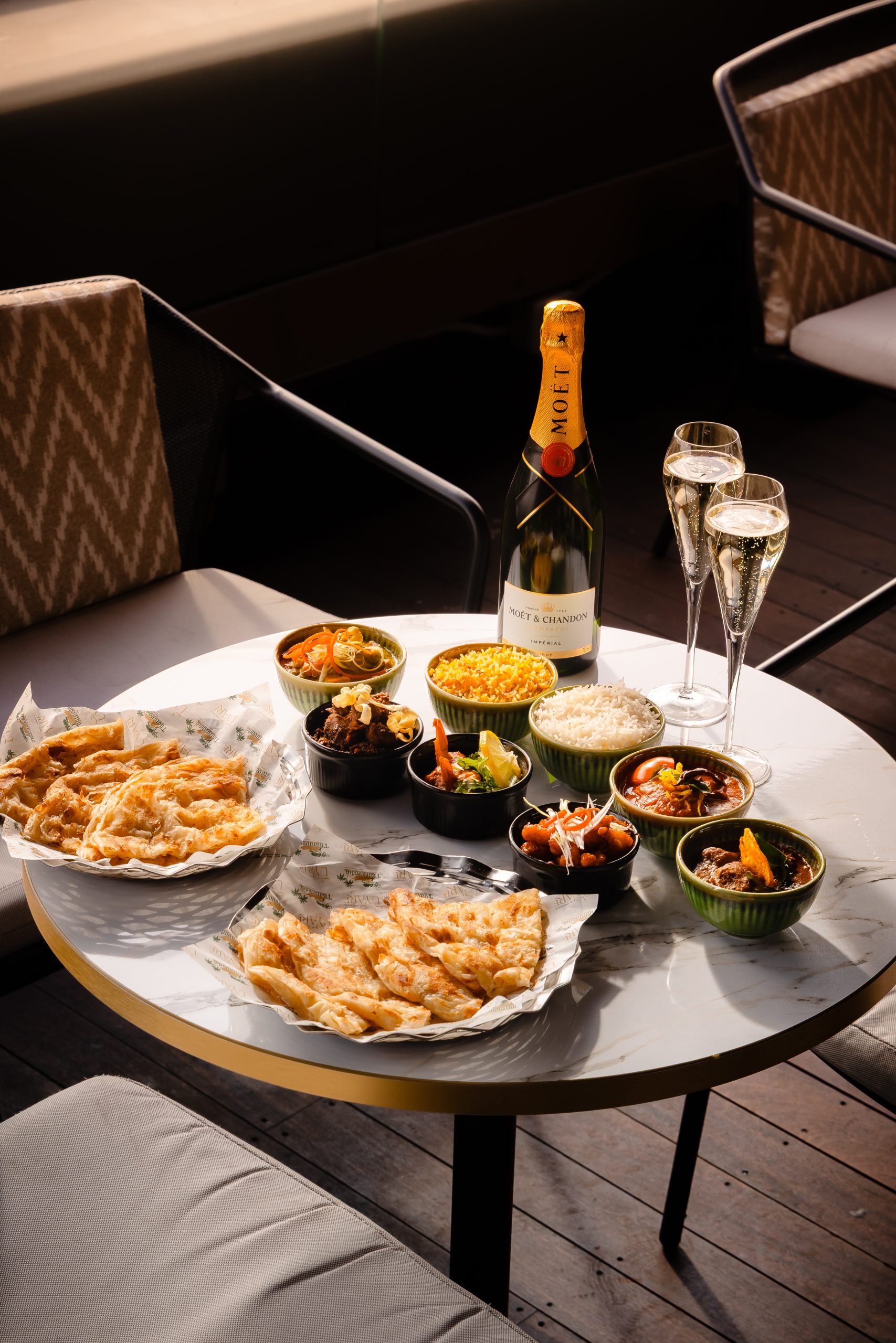 a small round table with plates and bowls of various food, a bottle of champagne and two champagne flutes