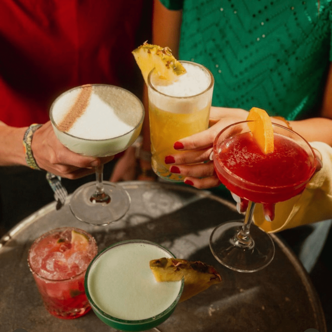 a table with a variety of cocktail glasses and drinks with hands reaching for each glass