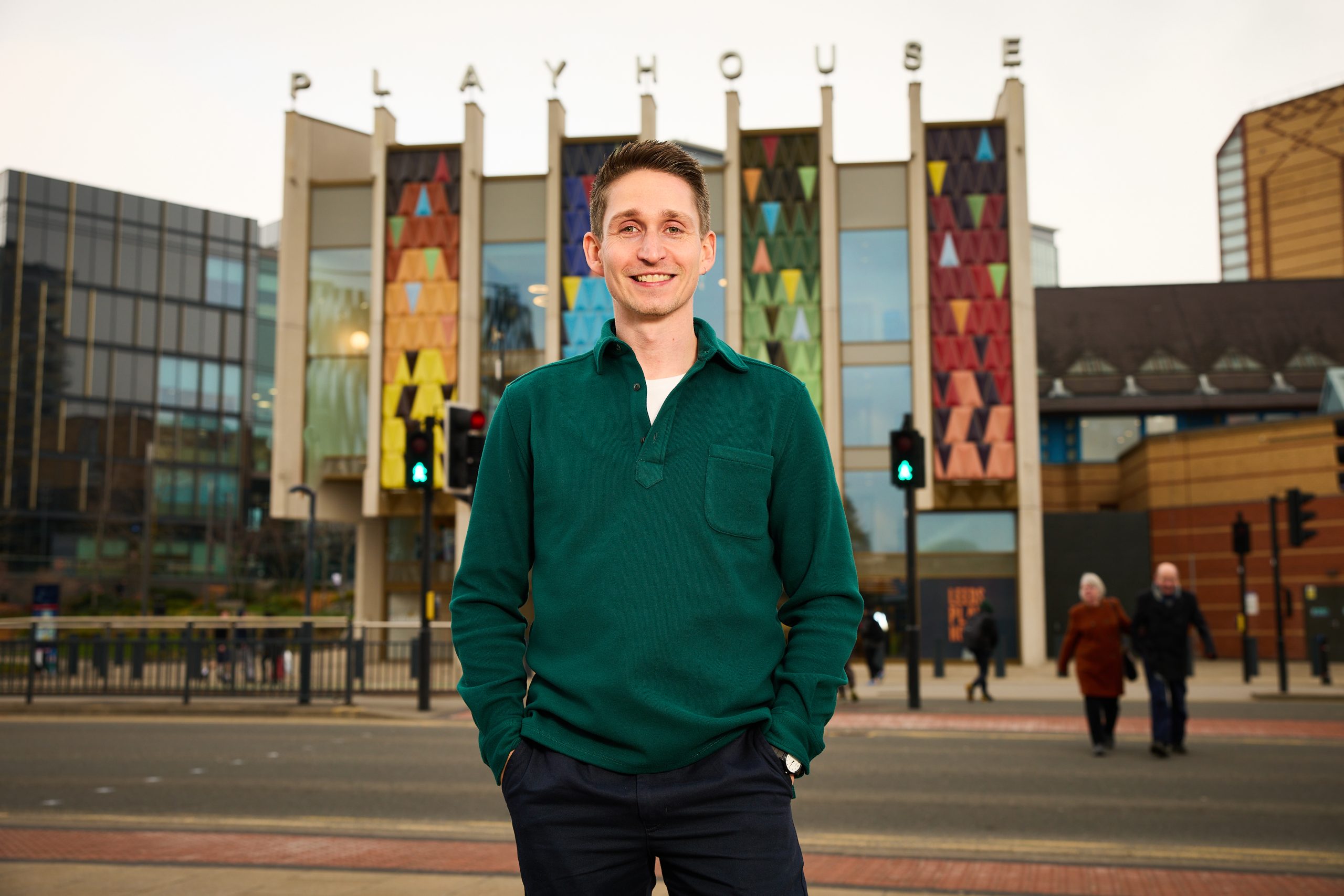 a person stood on a path smiling at the camera with a colourful building behind with the word playhouse on the top