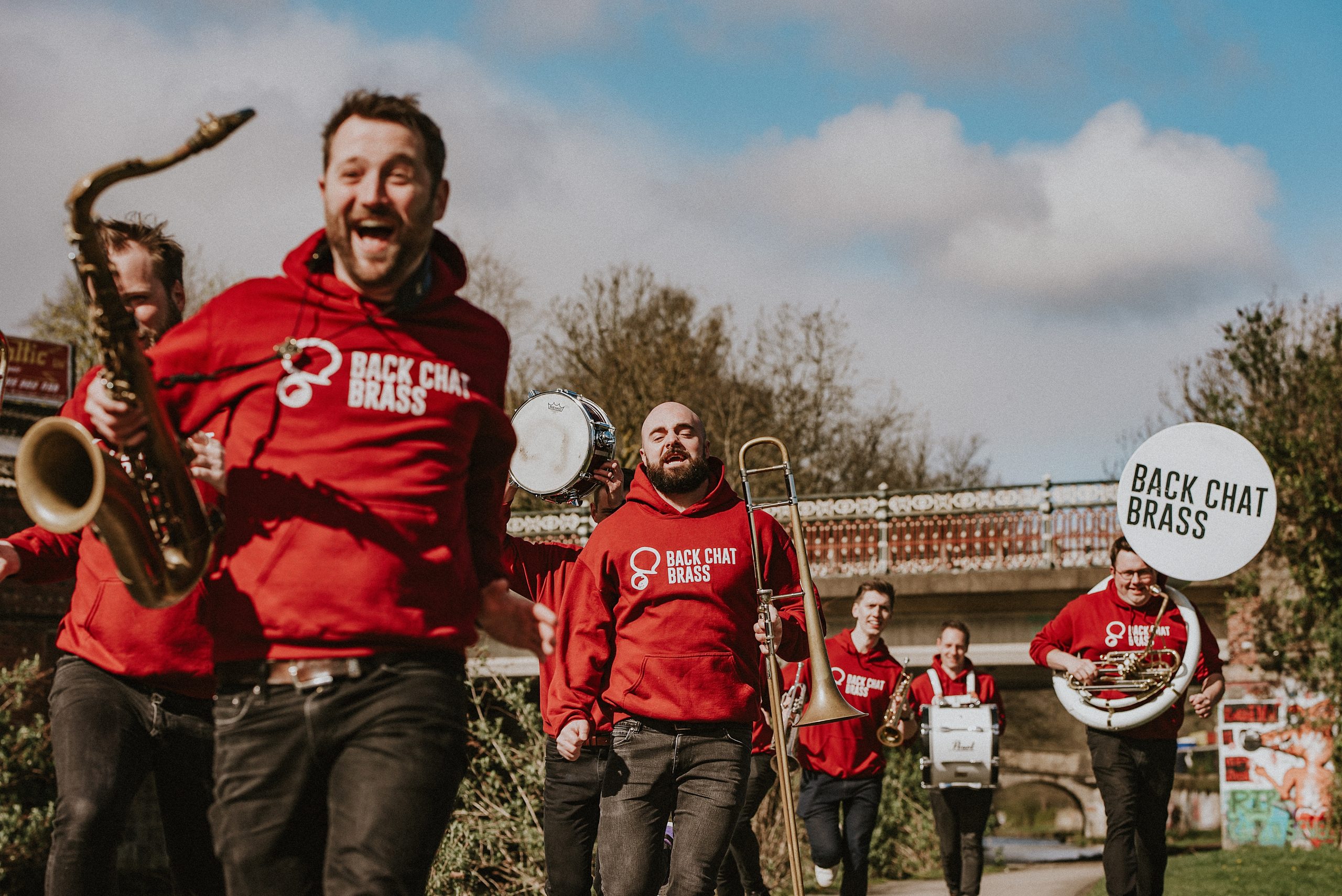 a group of people outside in red hoodies holding a variety of brass instruments