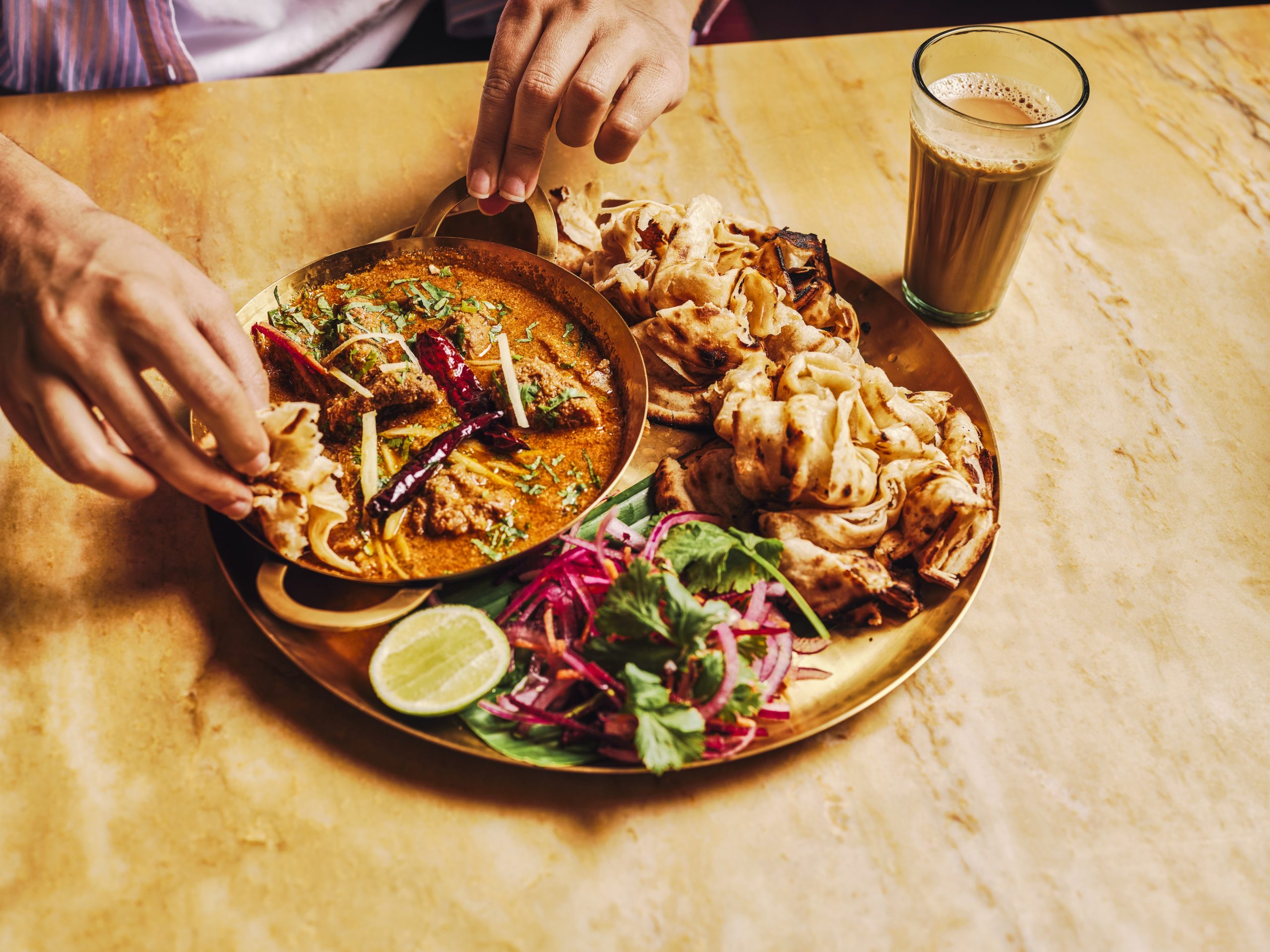 a plate of curry with a drinking glass next to it, and a person reaching out to eat the food