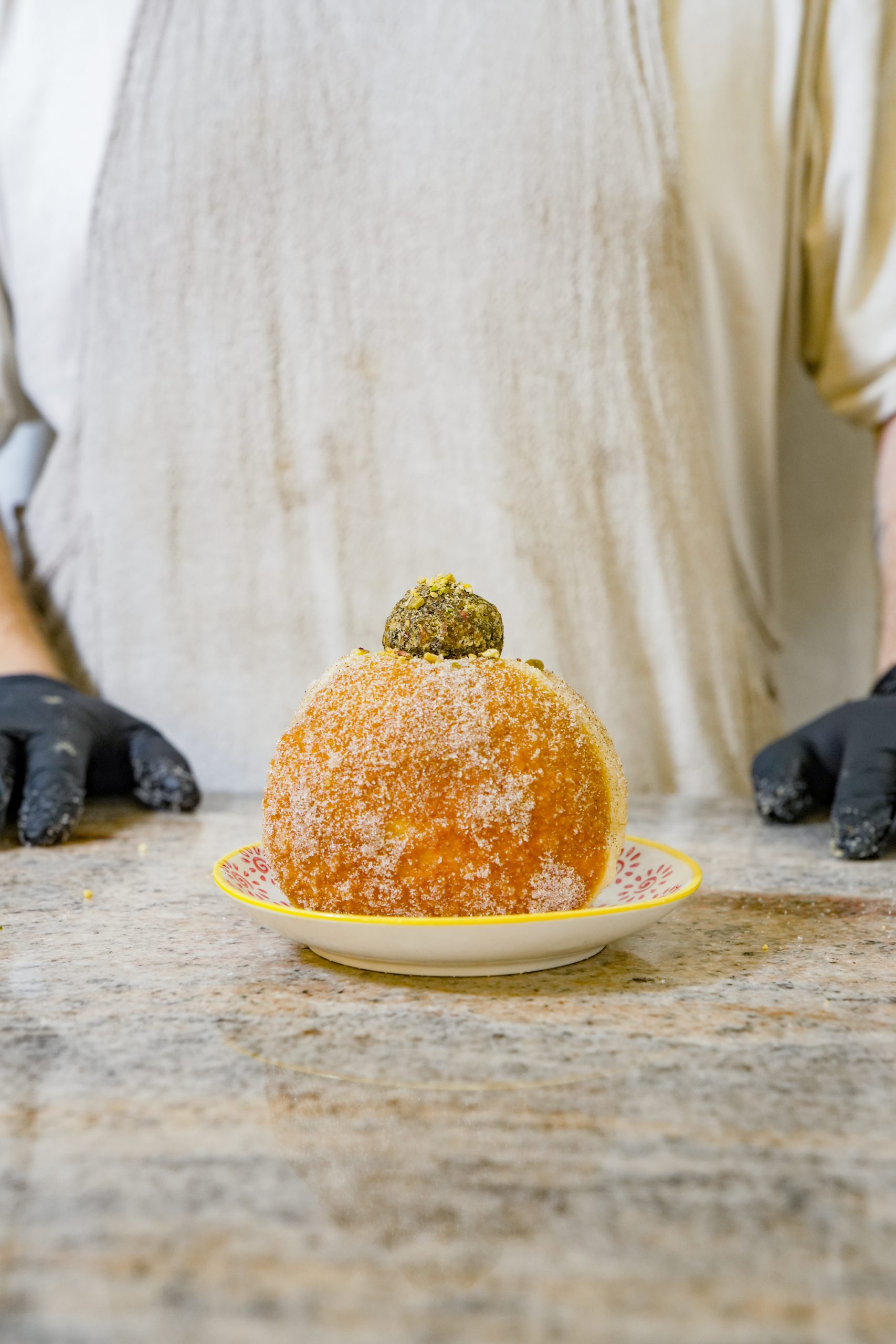 a chef in an apron standing behind a table with a donut on a plate