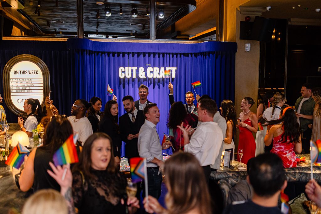 an interior shot with a crowd of people holding rainbow pride flags 