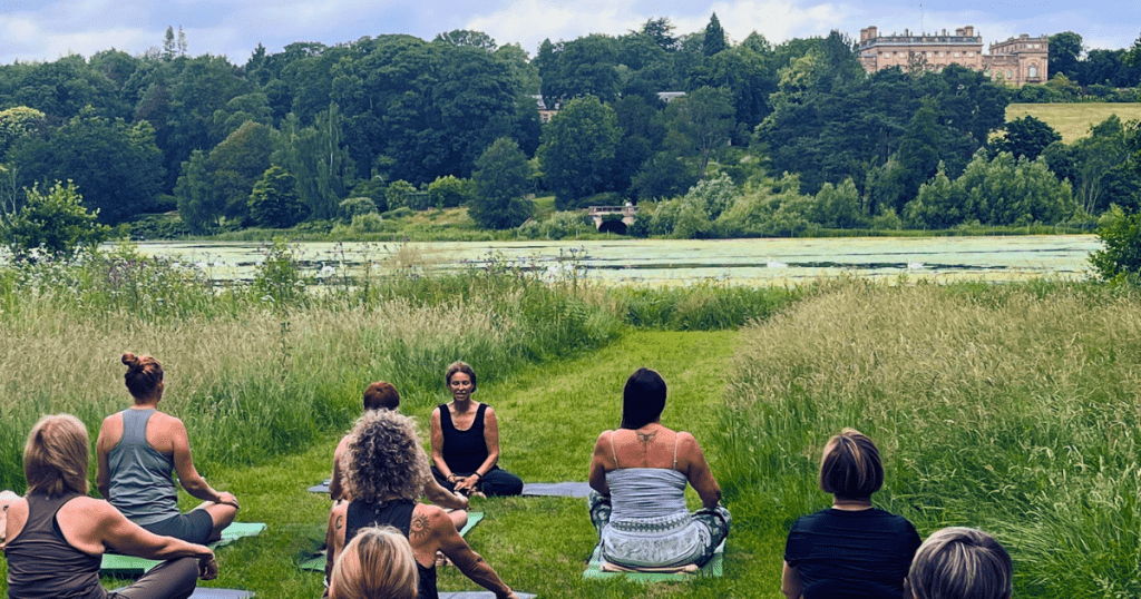 A group of people meditating in seated, relaxed yoga pose in the grounds of Harewood House.