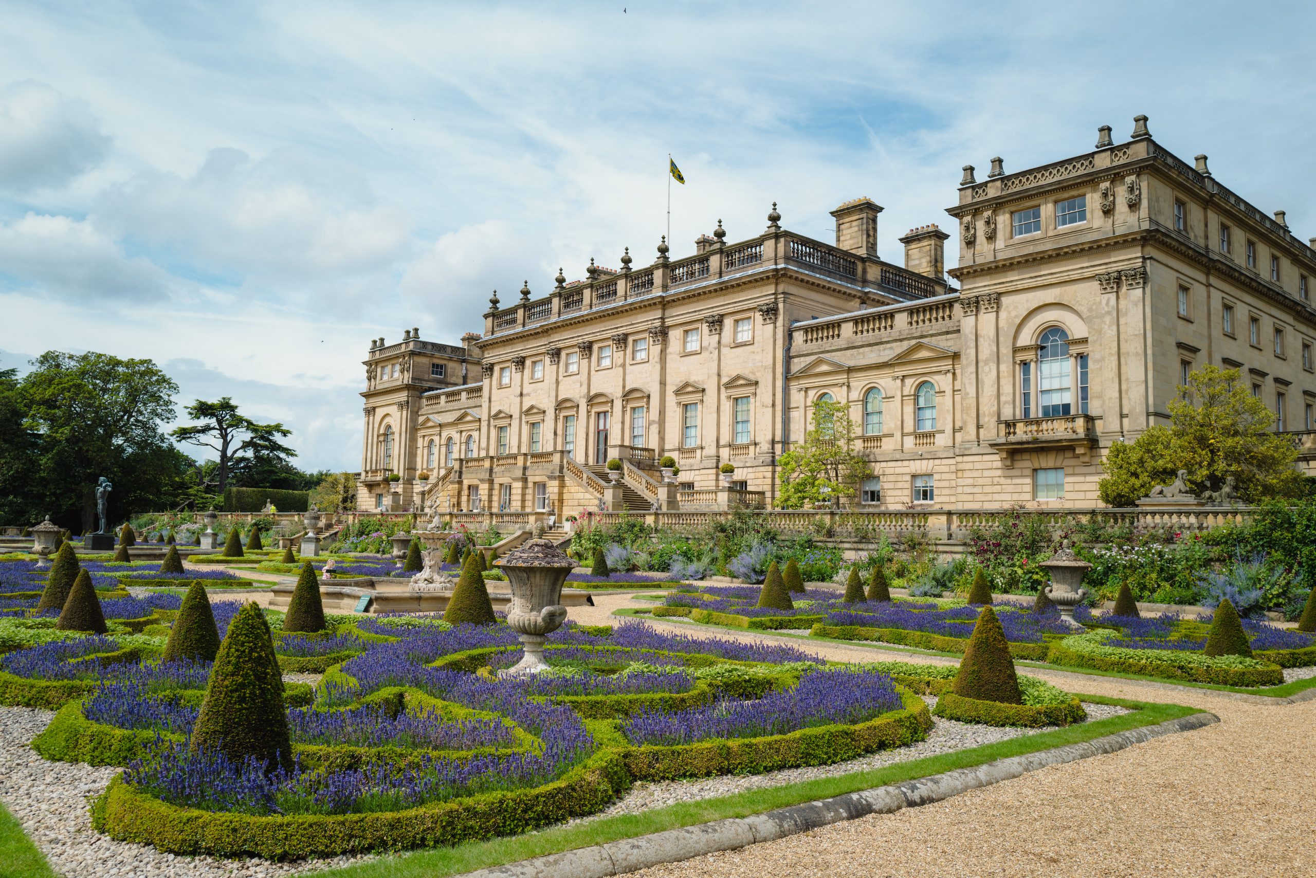 the exterior of a large historic home with a manicured garden of bushes and flowers in front