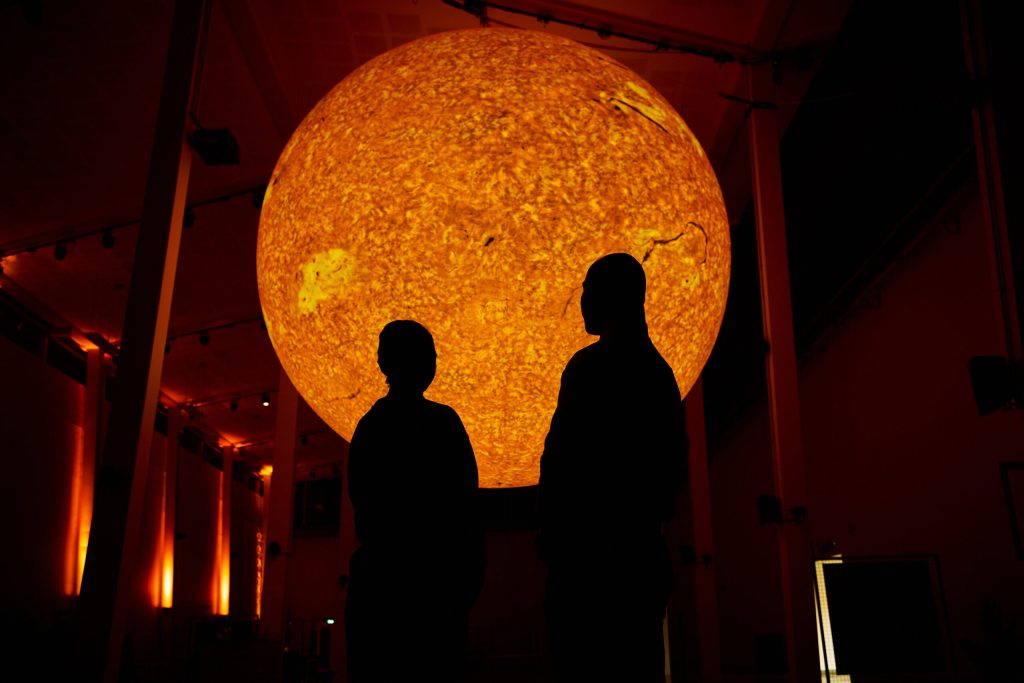 people stood in a dark room with a large spherical light imitating the sun