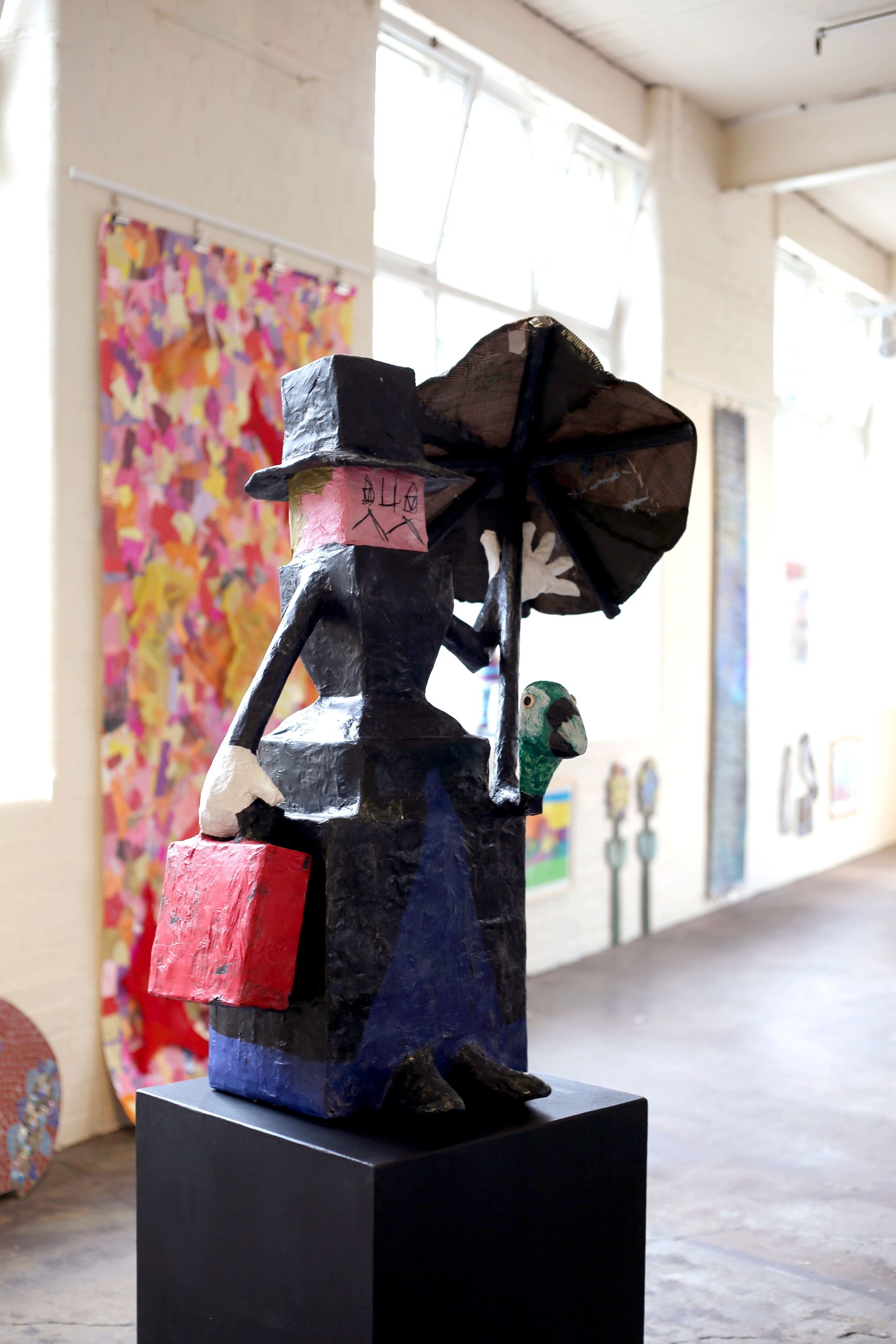 a sculpture of a woman holding an umbrella and a large handbag in a dress and with a black hat on