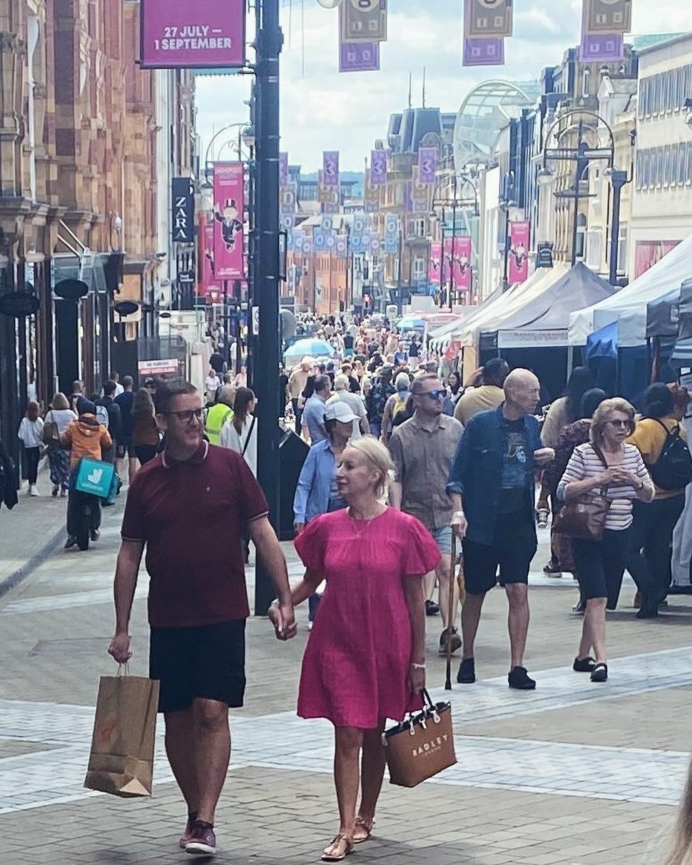 a long wide street with people walking up and down holding shopping bags and a line of market tents through the middle
