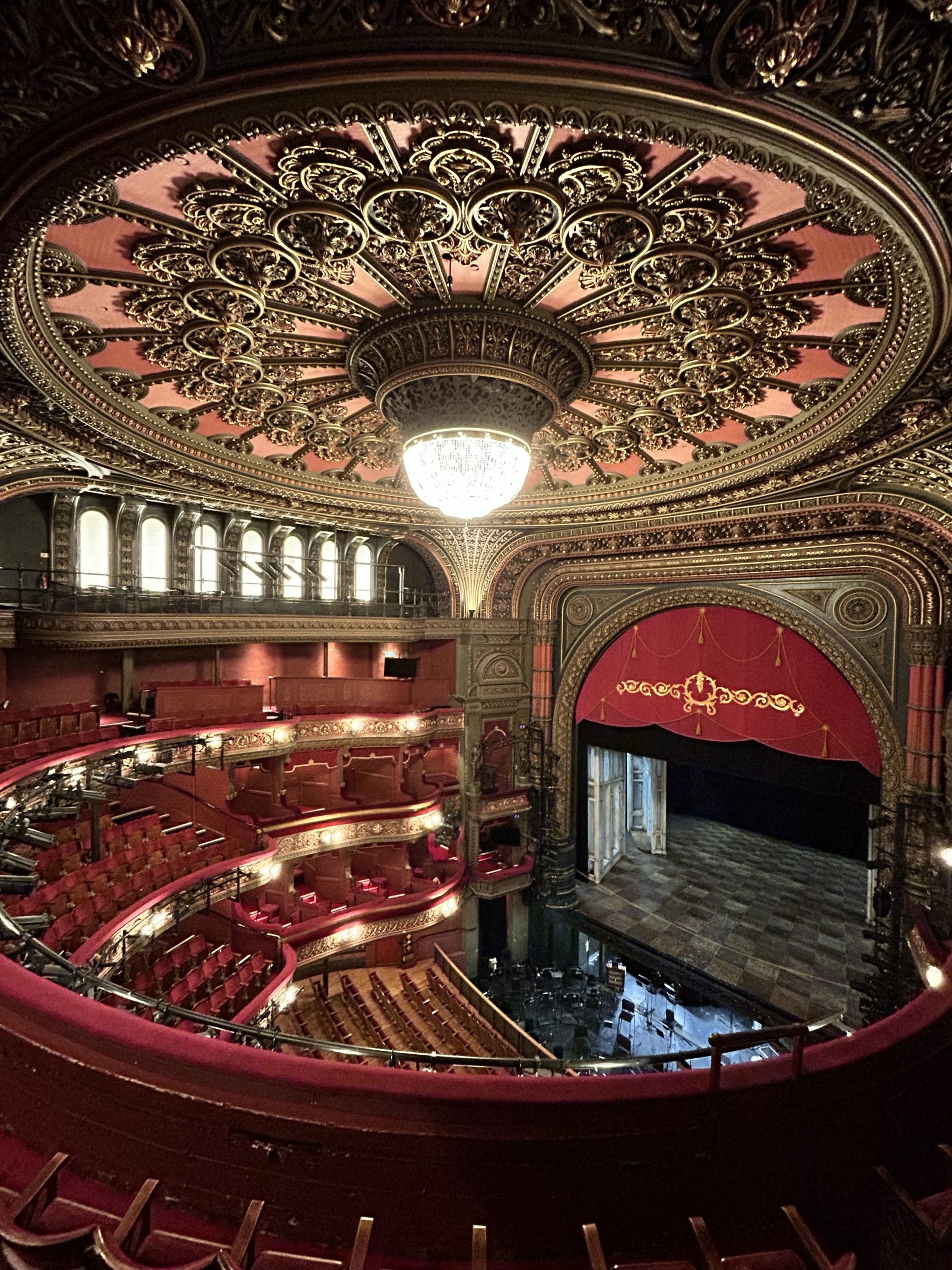 the interior of a theatre with four floors, a large stage, red velvet seating and golden accents
