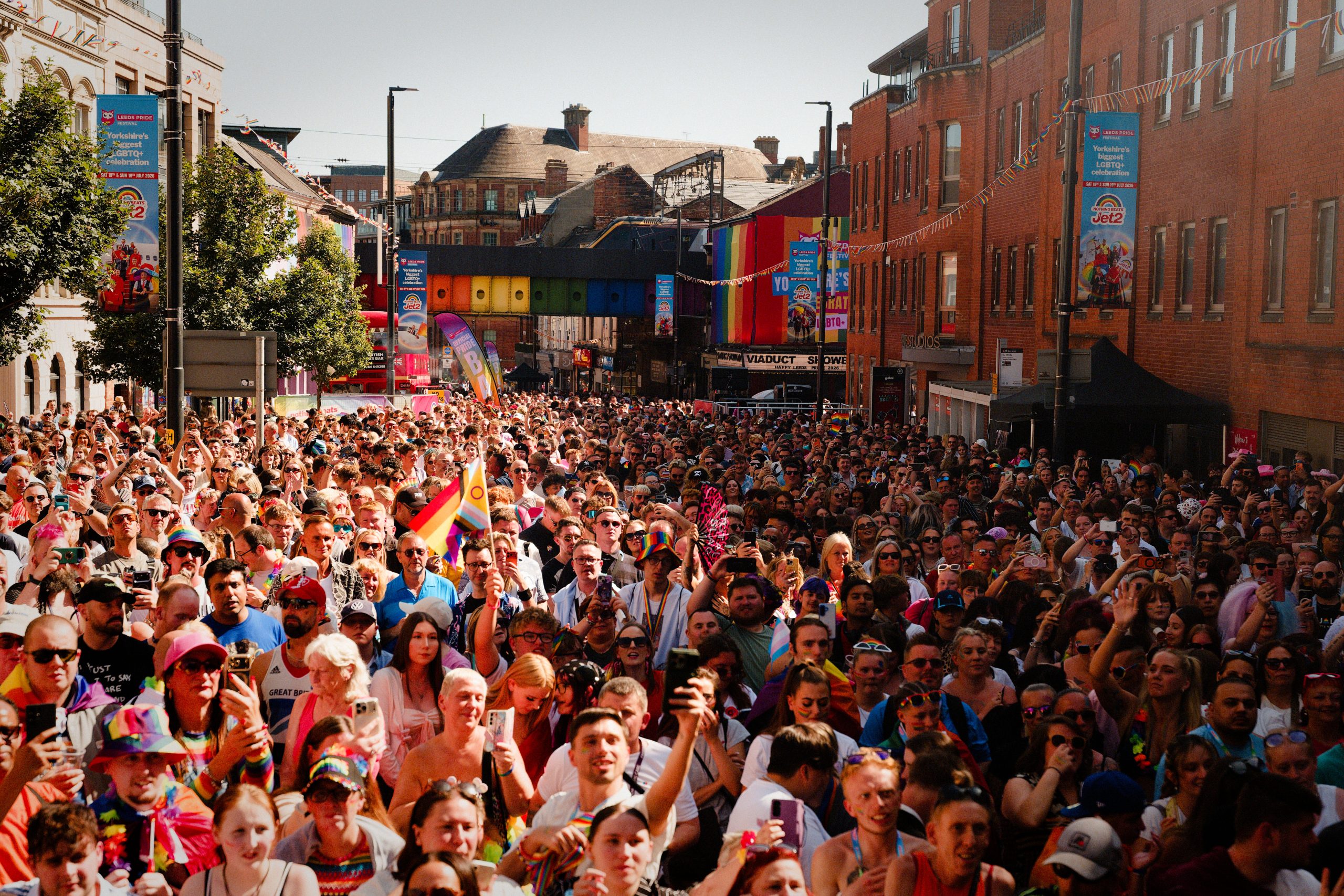 a large crowd in the middle of a street waving colourful pride flags