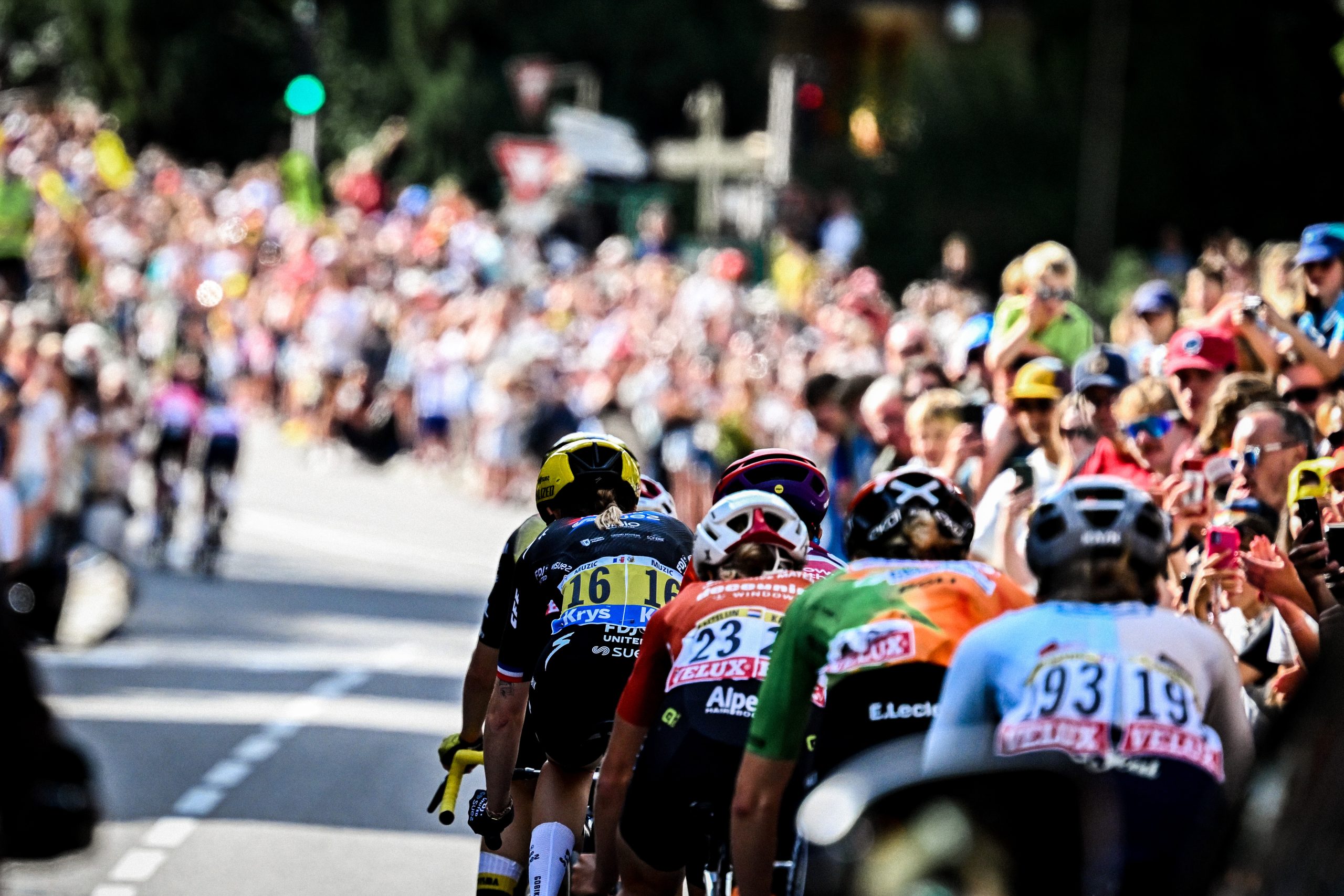 a line of professional cyclists moving towards a crowd of people