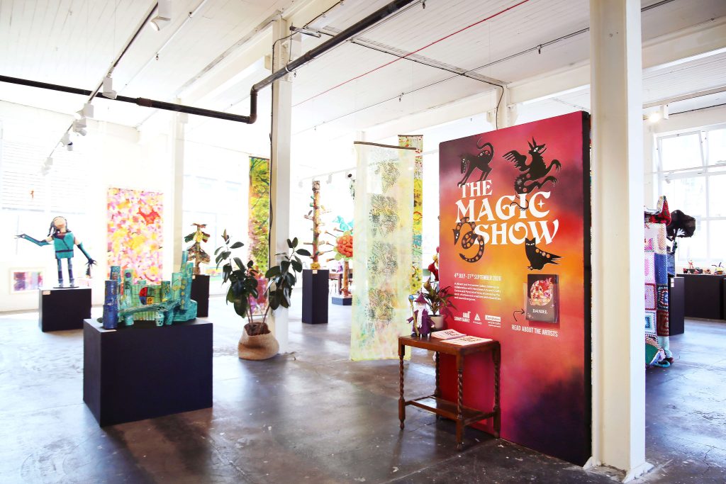 an exhibition hall with a banner saying the magic show, and a range of podium with objects