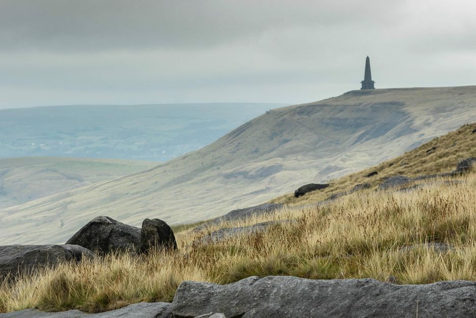 a long view over a moor landscape with a stone spire in view far away