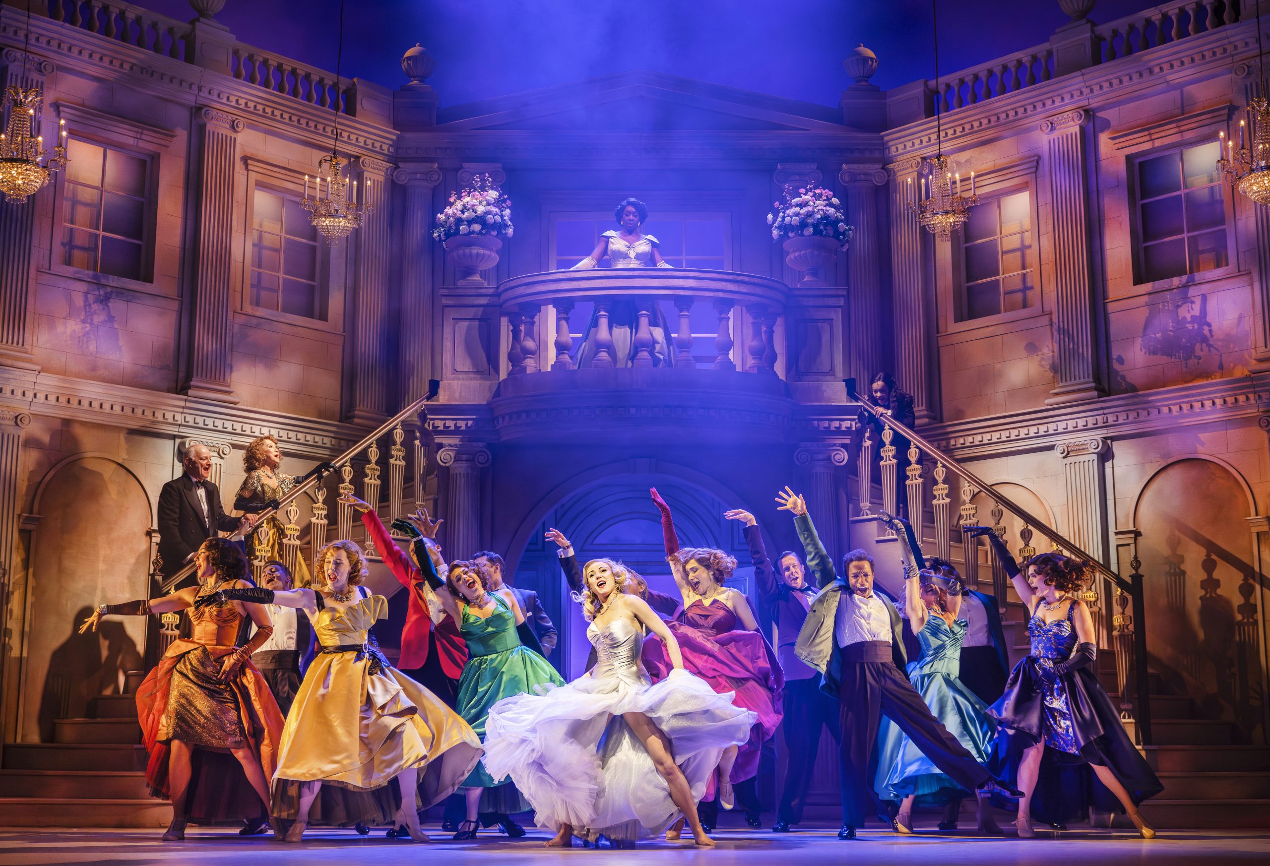 a theatre stage featuring a staircase, with people dancing in colourful dresses at the bottom