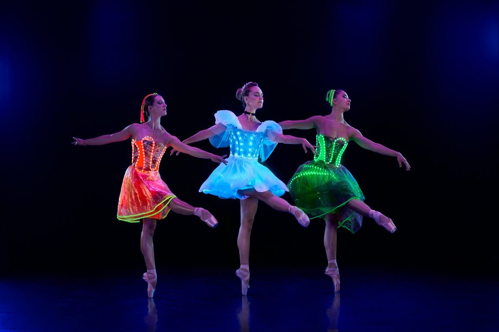 three female ballet dancer in a dark room, with light up dresses in different colours