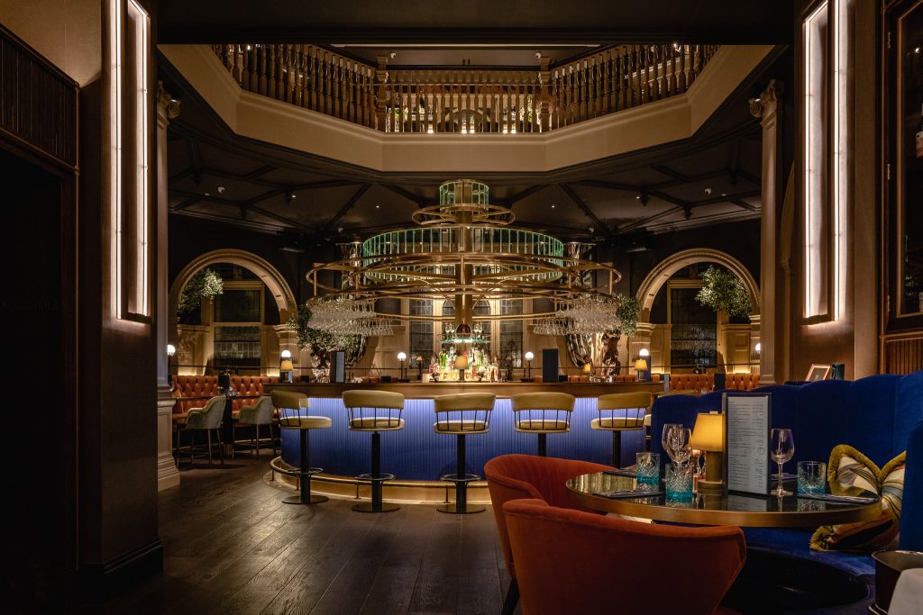 View of cut and craft with bar in centre and up-lit velvet blue bar stools.