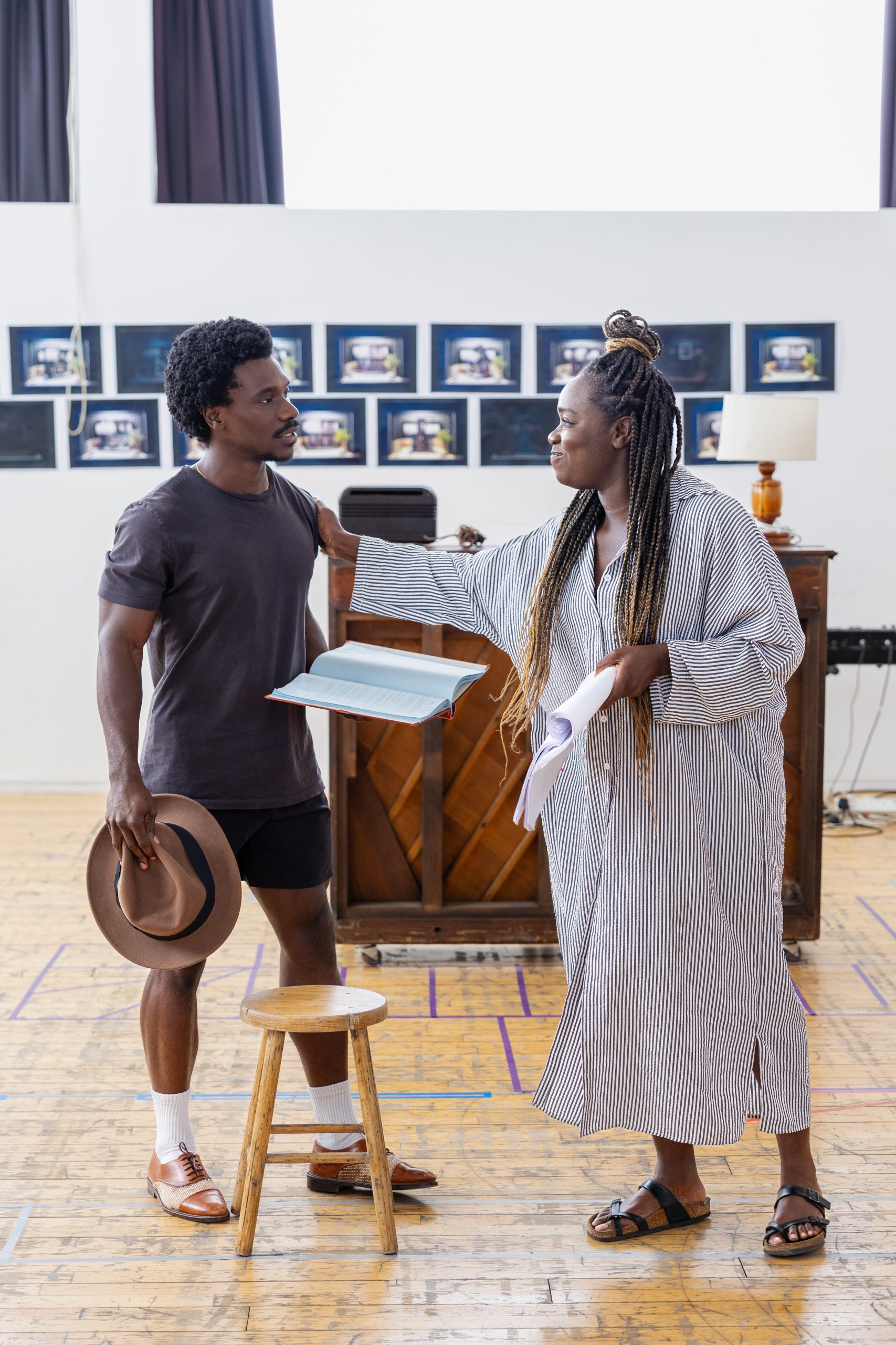 two people stood in a room holding pieces of paper, one holding a hat and a piano behind them