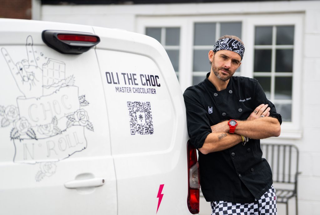 a man in a chefs coat and a bandana leaning on the back of a white van