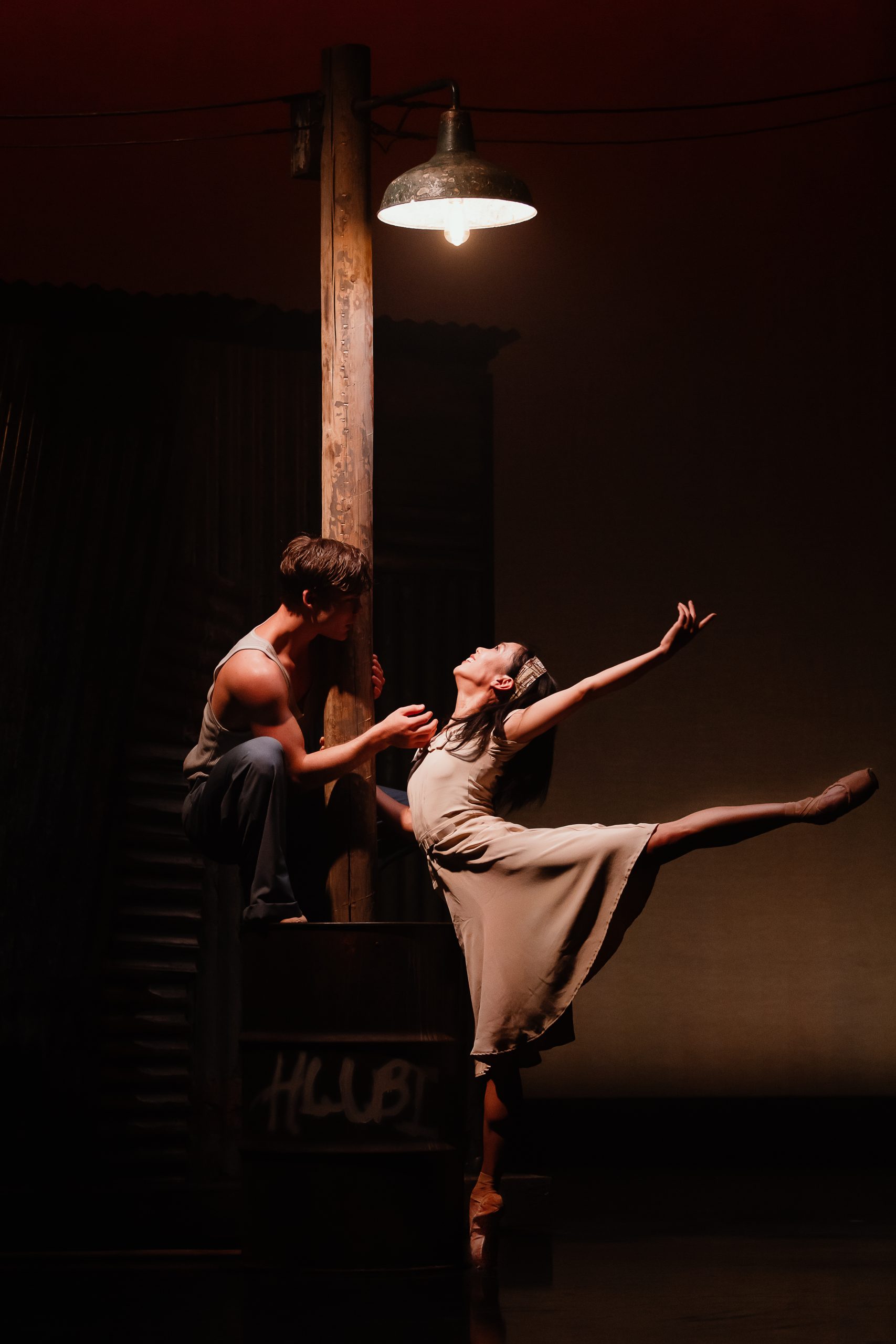two ballet dancers on a dark stage with a light overhead lighting just them