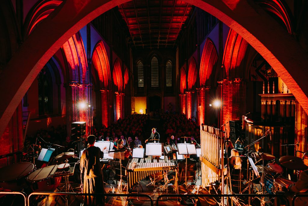 an orchestra in a dark church lit up with low lights, performing for a crowd