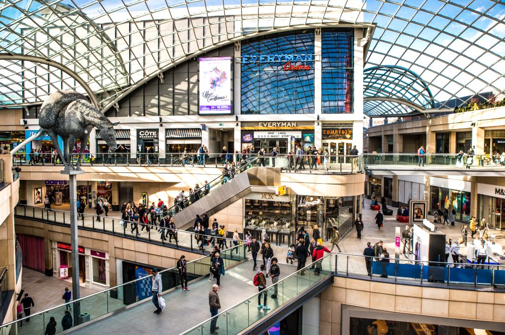 a large shopping centre with a glass roof and three floors with people walking around