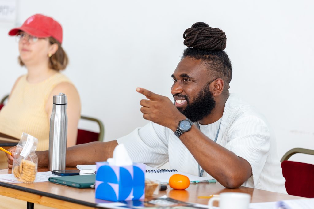 two people sat at a table with several items laid out including waterbottles, a box of tissues and paper